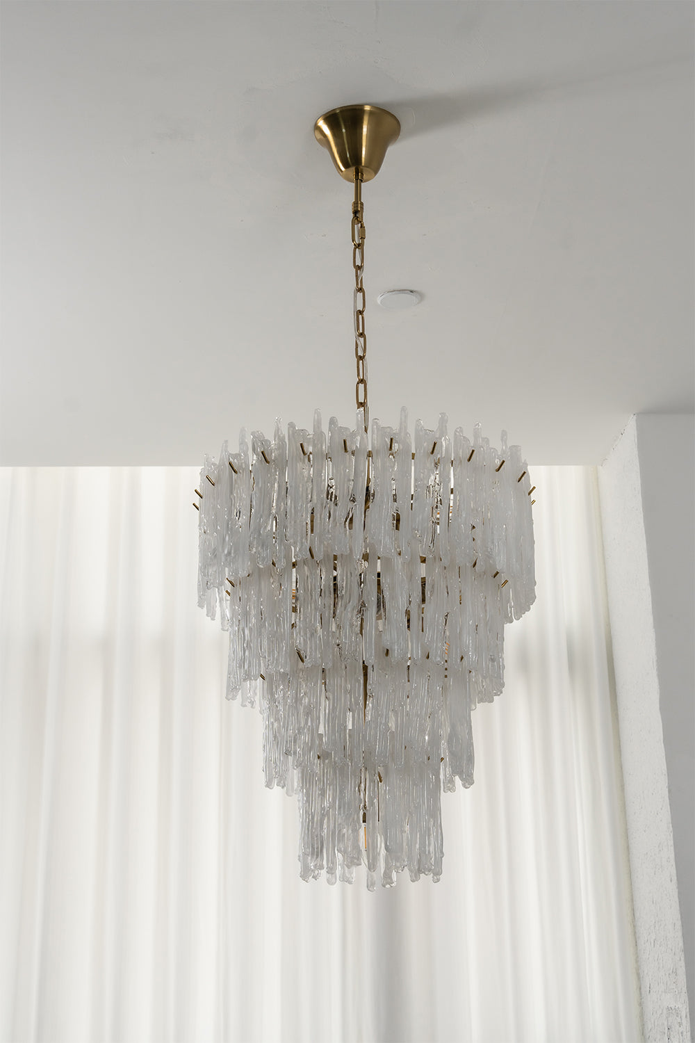 Ethereal Icicle Waterfall Chandelier | Glass, Metal | Unlit view of the tiered glass chandelier showcasing its crystalline elegance in front of sheer white blinds | vexa lamps