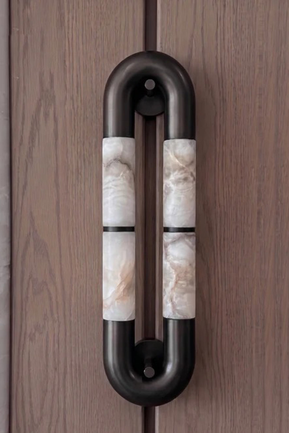 Evadne Alabaster Link Wall Sconce | Alabaster, Metal | Sconce unlit or in dim lighting mounted vertically on a dark wood-paneled wall, showing its architectural pill-shaped outline | vexa lamps