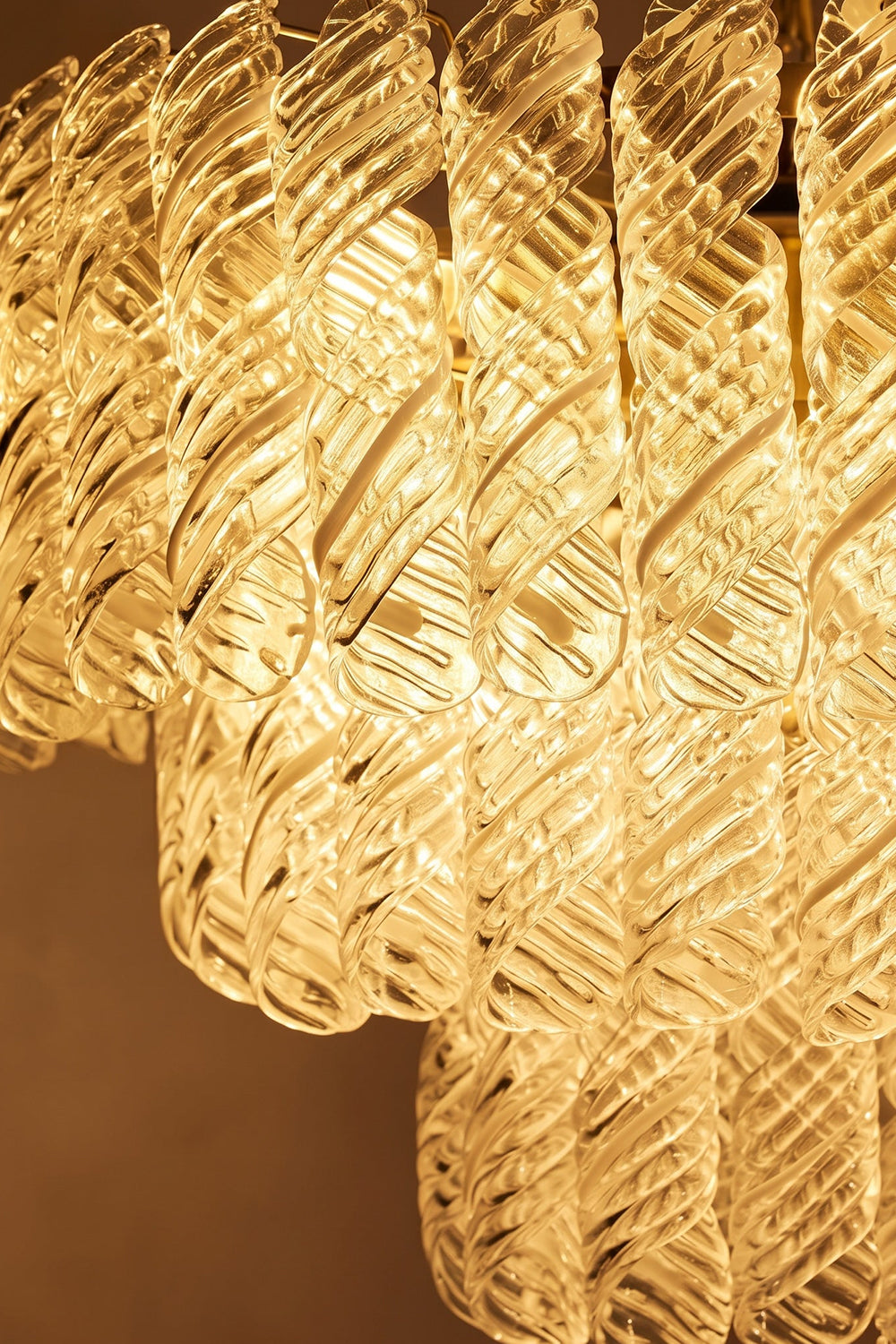Evangeline Tiered Twisted Glass Chandelier | Illuminated Glass Detail | Close-up macro view of the fully lit clear twisted glass cylinders showcasing the warm golden light refraction | Detail shot | vexa lamps