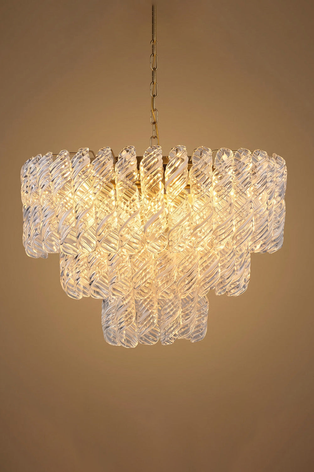 Evangeline Tiered Twisted Glass Chandelier | Studio Lit Presentation | Fully lit tiered luxury glass chandelier casting a deep warm golden halo against a neutral beige background | vexa lamps