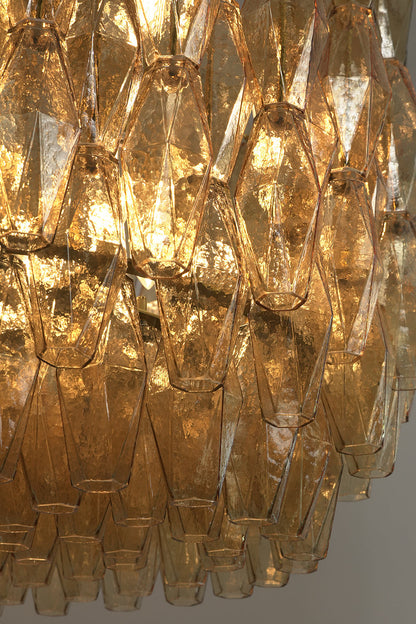 Low-angle view of lit amber glass chandelier | Metal, Glass | Showing the layered drum structure and warm light | vexa lamps