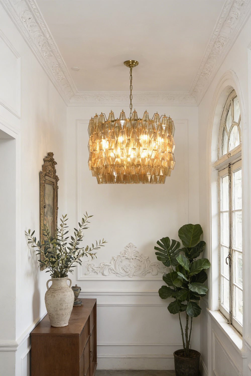 Luxurious amber glass drum chandelier | Metal, Glass | Hanging in a hallway with white wainscoting and plants | vexa lamps