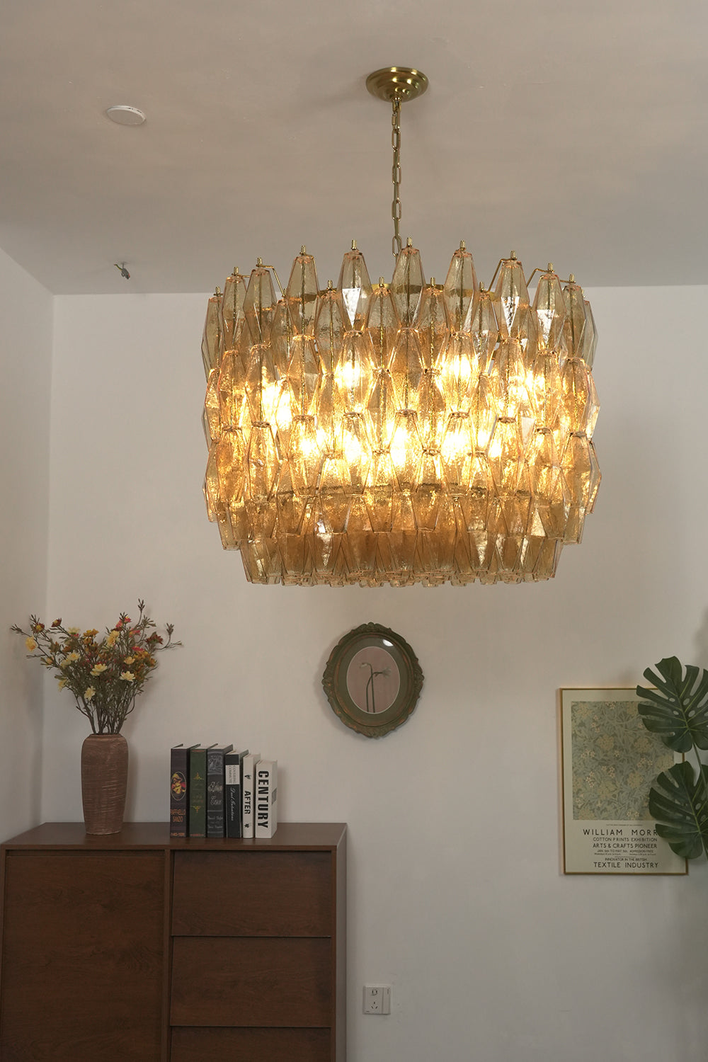 Lit amber drum Sorrento chandelier | Metal, Glass | Mounted above a dark wooden cabinet in a living room | vexa lamps