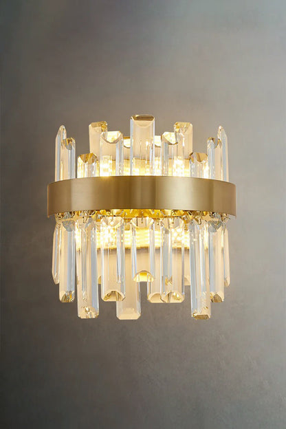 Glacia Tiered Crystal Statement Wall Lamp | Crystal, Metal | Studio front view of the fully illuminated crystal sconce casting a rich warm light halo on a dark textured grey background wall | vexa lamps