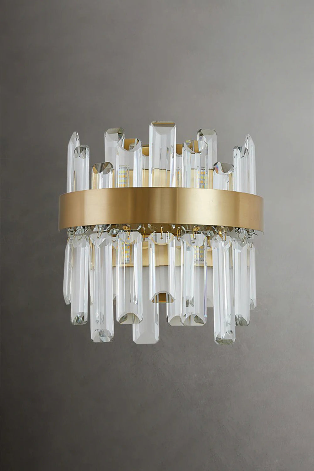 Glacia Tiered Crystal Statement Wall Lamp | Crystal, Metal | Unlit studio view of the modern crystal wall lamp showcasing the glass clarity and gold metal hardware against a dark grey background | vexa lamps