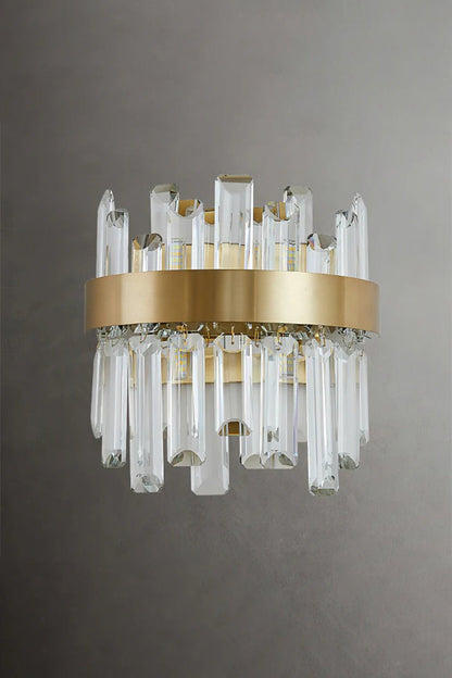 Glacia Tiered Crystal Statement Wall Lamp | Crystal, Metal | Unlit studio view of the modern crystal wall lamp showcasing the glass clarity and gold metal hardware against a dark grey background | vexa lamps