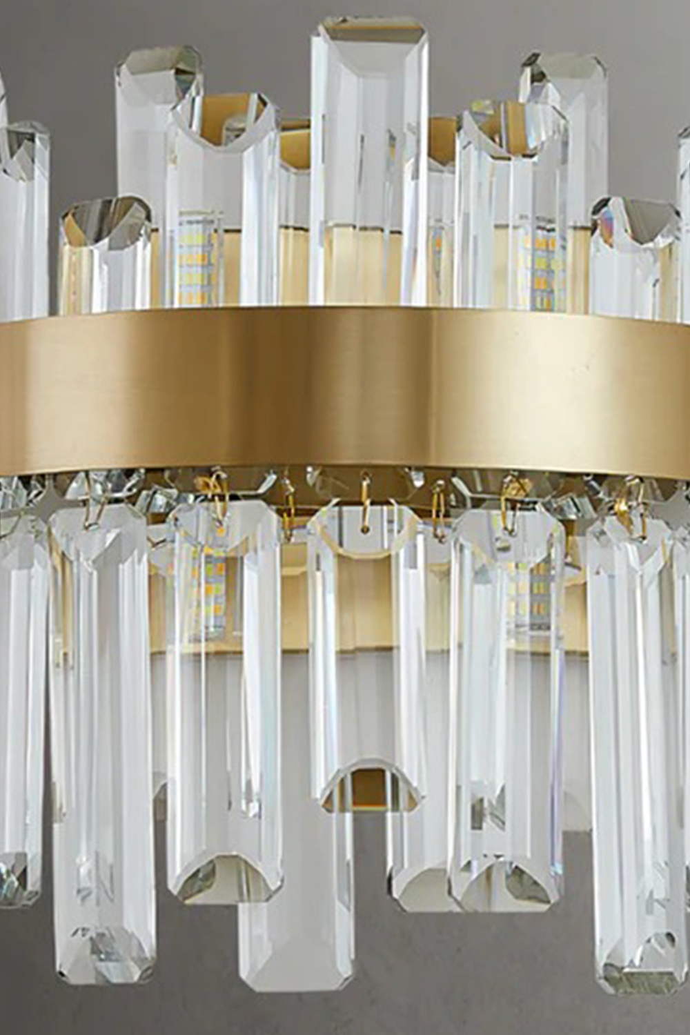 Glacia Tiered Crystal Statement Wall Lamp | Crystal, Metal | Detailed shot of the brushed satin finish on the gold metal band securing the two layers of transparent geometric crystal pillars | Detail shot | vexa lamps
