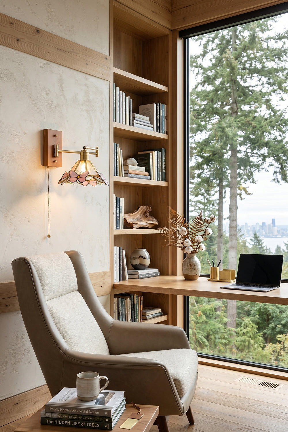 Iris Butterfly Stained Glass Wall Lamp | Stained Glass, Metal, Wood | Providing warm task light over a comfortable grey upholstered armchair and built-in wooden bookshelves facing a scenic forest window | vexa lamps