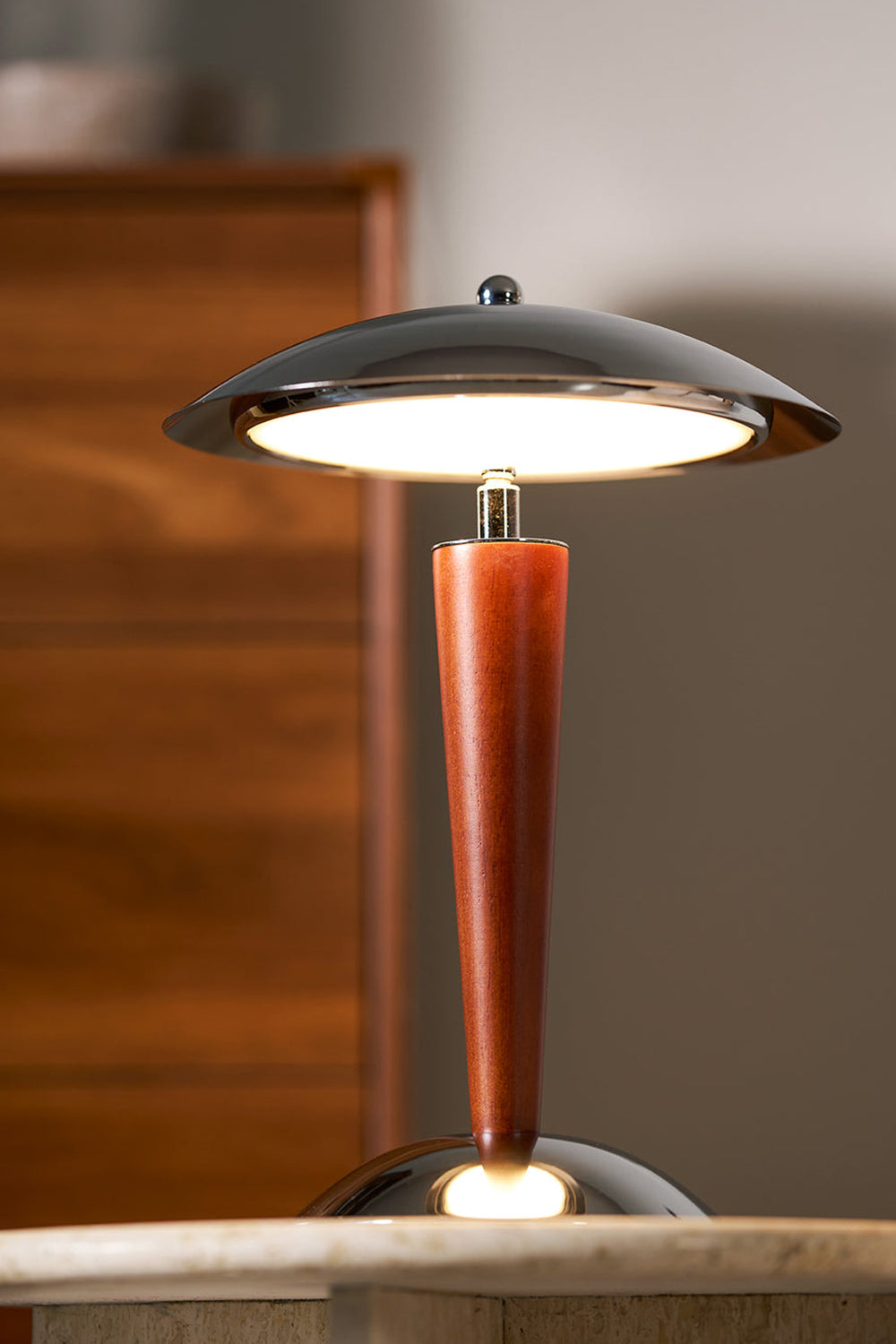 Isolde Domed Walnut Table Lamp | Cozy Accent Glow | Staged view of the fully illuminated mushroom lamp casting a warm yellow halo against a dark blurred wooden chest background | vexa lamps