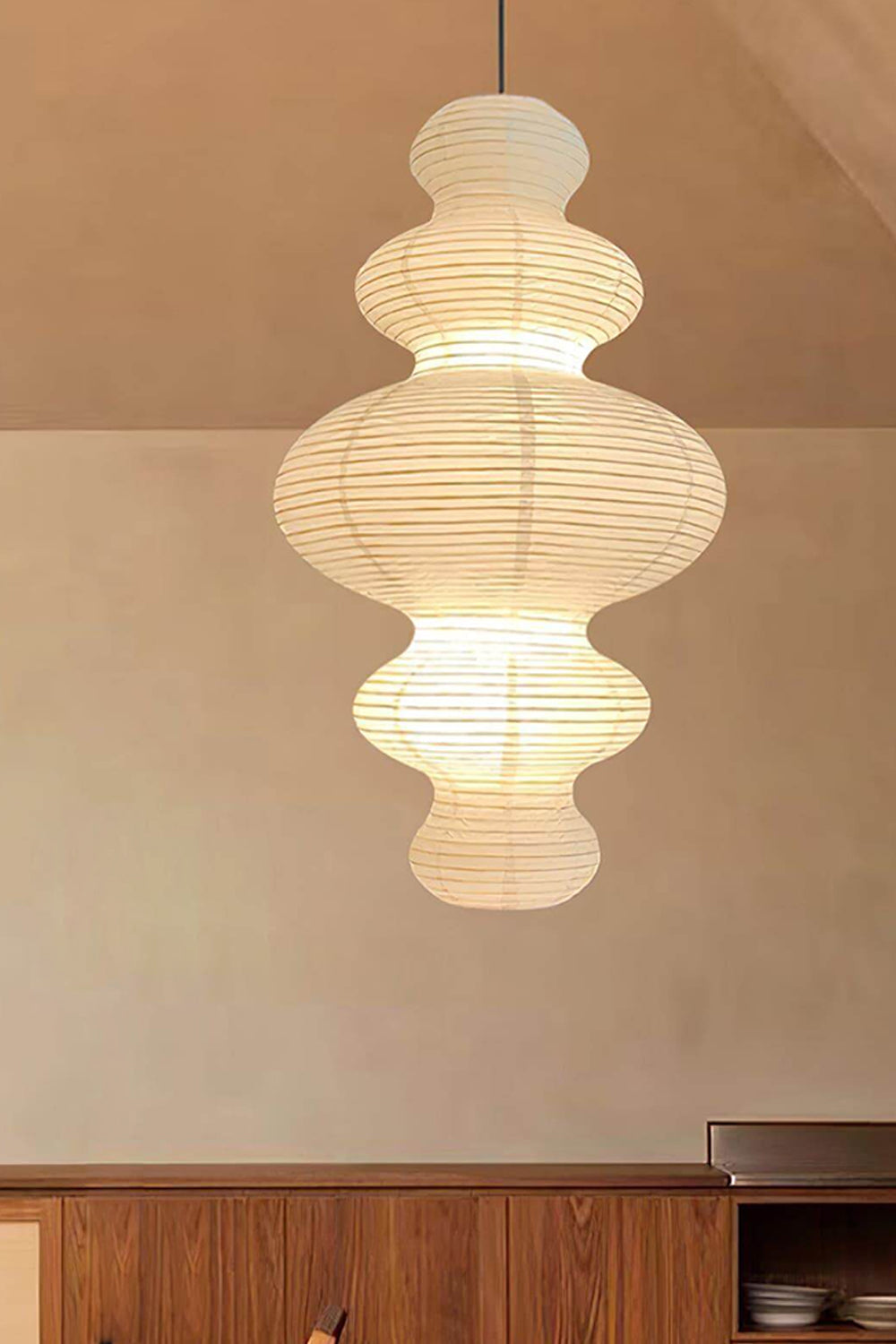 Isolde Stacked Paper Pendant Lamp | Textured Ribbed Paper | Suspended above a classic dark wood storage cabinet against a minimalist beige wall | vexa lamps