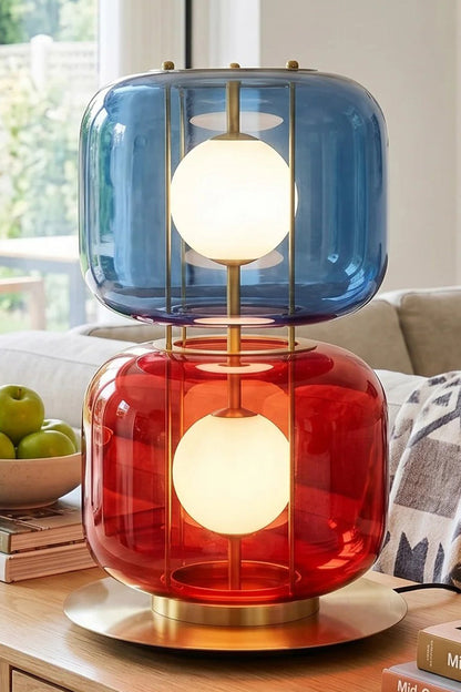 Jasper Colorblock Table Lamp | Glass, Metal | Fully lit blue and red glass stacked accent lamp standing on a wooden surface in a cozy contemporary residential living space | vexa lamps