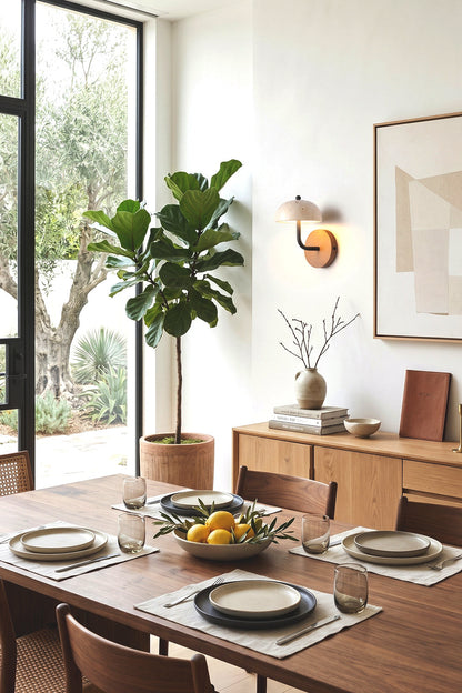 Koba Travertine Mushroom Wall Lamp | Travertine, Wood, Metal | Providing warm ambient lighting on a wall adjacent to a long wooden dining table and a large fiddle-leaf fig tree | vexa lamps