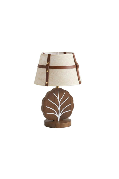 Leafora Botanical Leaf Table Light | Wood, Fabric, Leather | Isolated view of a rustic cottage-style table lamp featuring a cream woven fabric drum shade wrapped in brown leather straps on a sculpted wooden leaf-shaped base with white inlaid veins | White background | vexa lamps