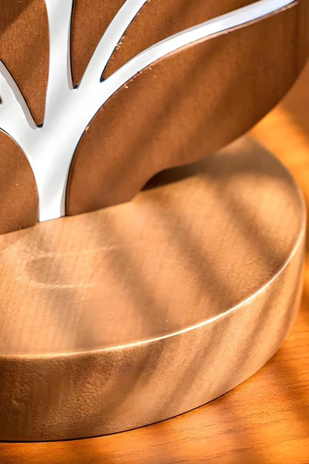 Leafora Botanical Leaf Table Light | Wood, Fabric, Leather | Macro close-up view of the sculpted warm brown wood lamp base showcasing the clean white inlaid botanical leaf vein lines under golden sunlight stripes | Detail shot | vexa lamps