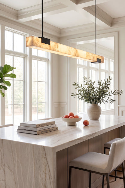 Liora Linear Alabaster Pendant Light | Natural Alabaster and Black Metal | Illuminating a modern white marble kitchen island bar counter with high ceiling windows | vexa lamps