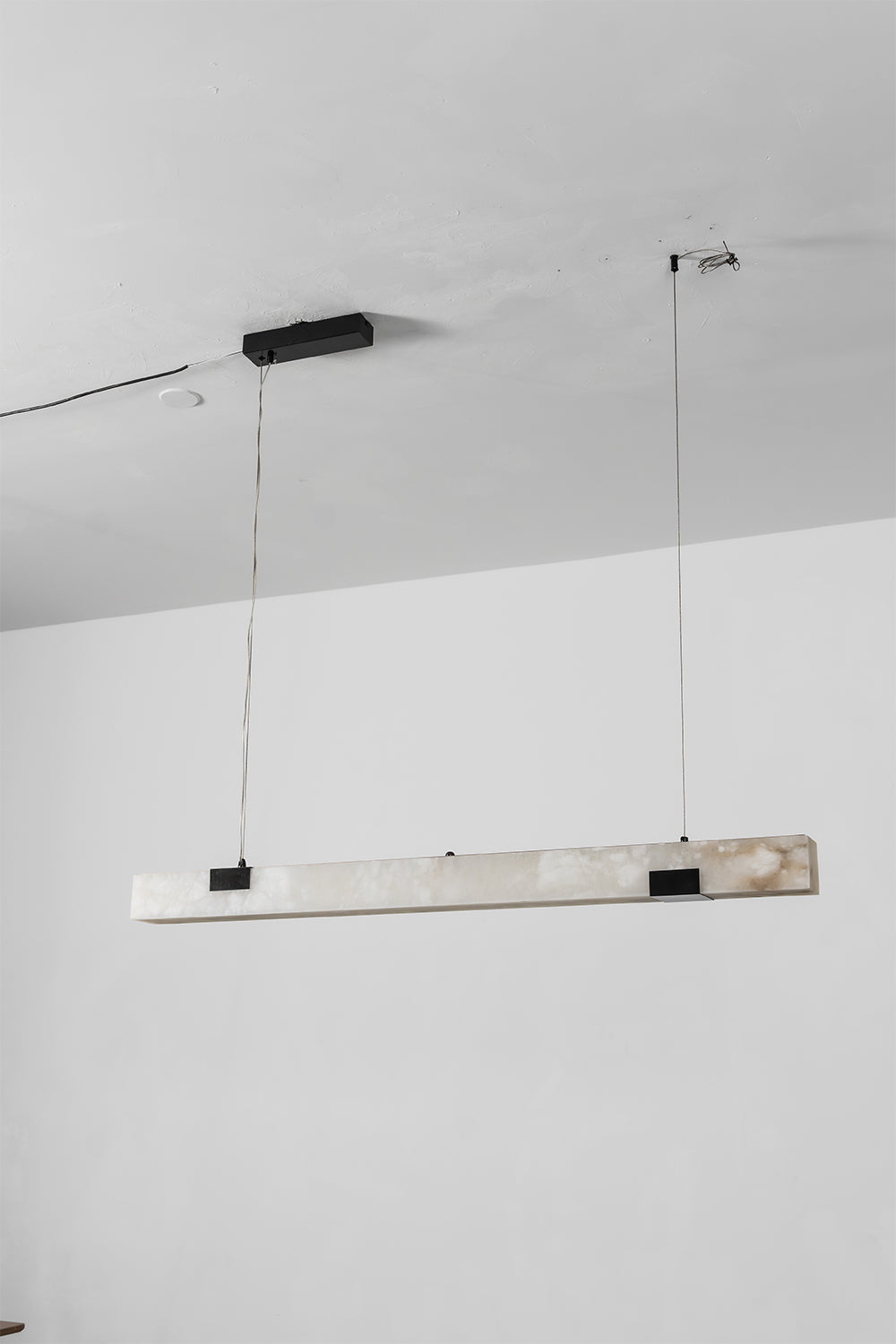 Liora Linear Alabaster Pendant Light | Natural Alabaster and Black Metal | Full studio product view of the unlit long linear fixture hanging from slim ceiling wires | vexa lamps