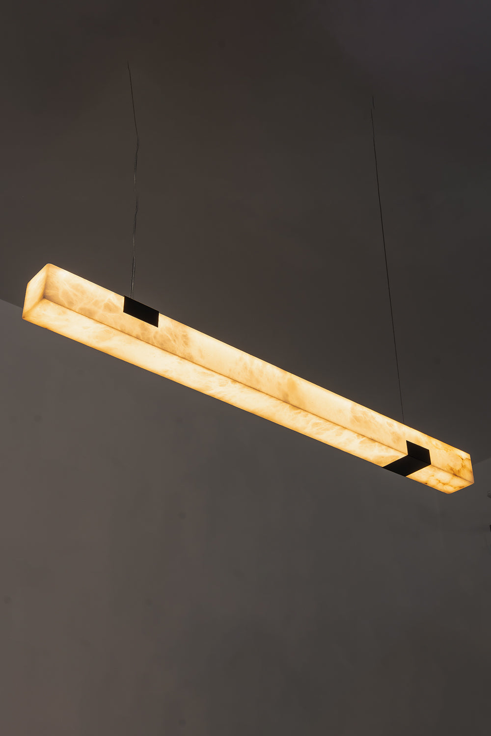 Liora Linear Alabaster Pendant Light | Natural Alabaster and Black Metal | High-angle view of the illuminated linear stone fixture glowing against a dark background | vexa lamps