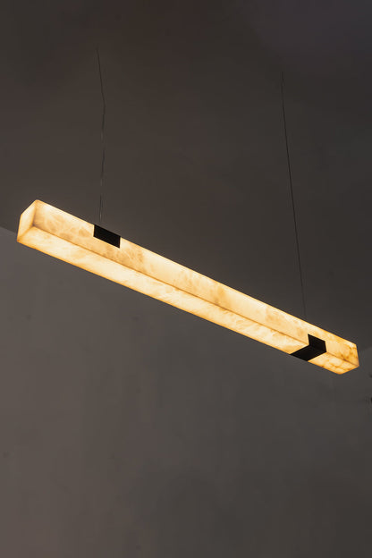 Liora Linear Alabaster Pendant Light | Natural Alabaster and Black Metal | High-angle view of the illuminated linear stone fixture glowing against a dark background | vexa lamps