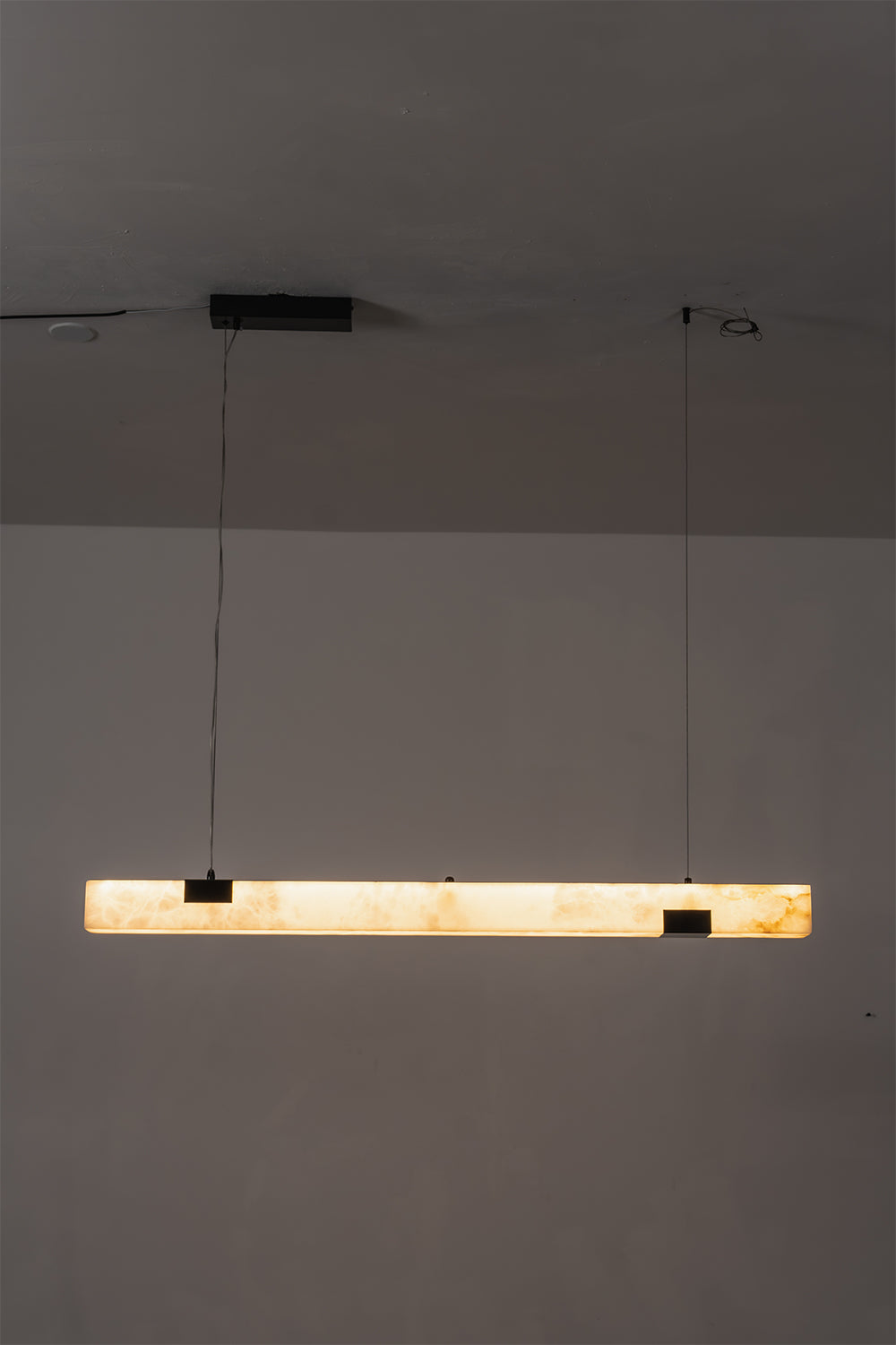 Liora Linear Alabaster Pendant Light | Natural Alabaster and Black Metal | Minimalist full view of the illuminated linear pendant light glowing in a dimly lit environment | vexa lamps