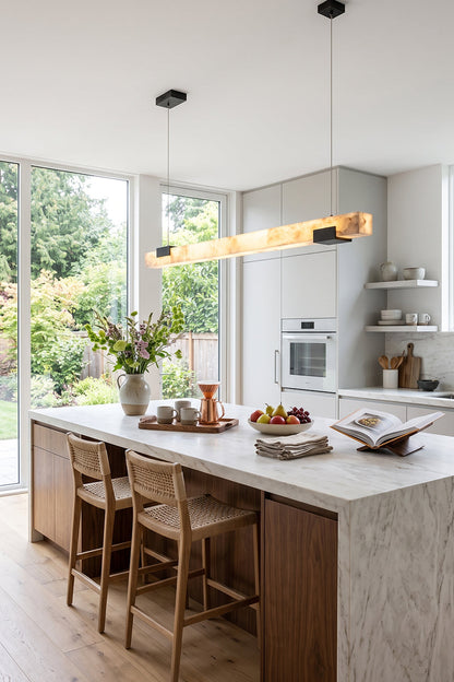 Liora Linear Alabaster Pendant Light | Natural Alabaster and Black Metal | Positioned over a long marble kitchen counter surrounded by matching wooden bar stools | vexa lamps