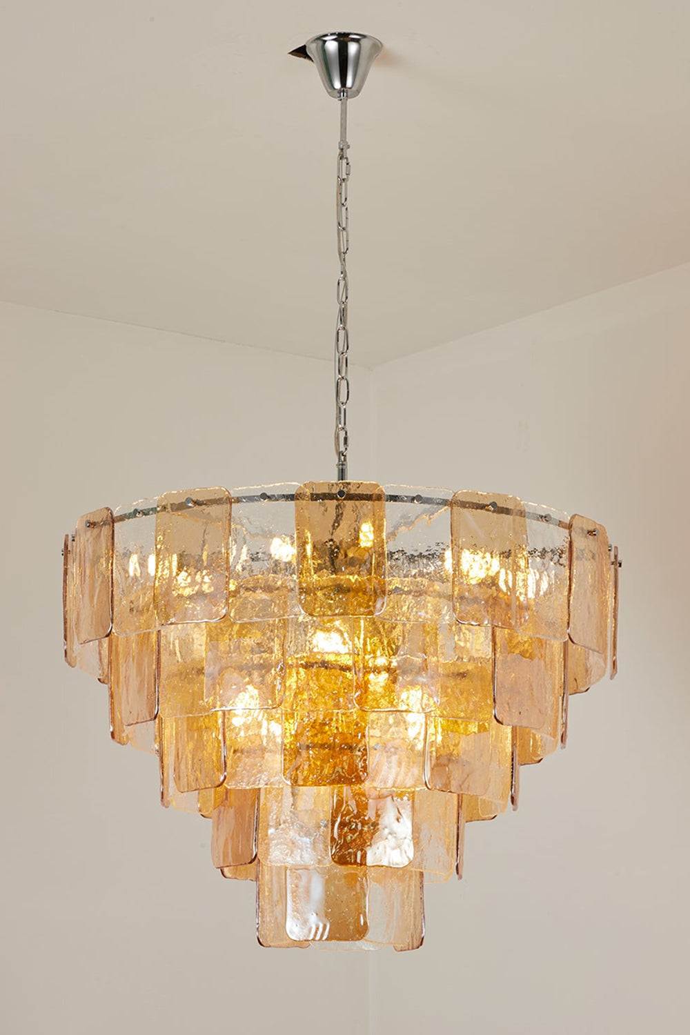 Lucia Tiered Amber Glass Chandelier | Glass, Metal | Alternative full studio shot of the illuminated tiered glass light fixture hanging elegantly against a grey studio backdrop | vexa lamps