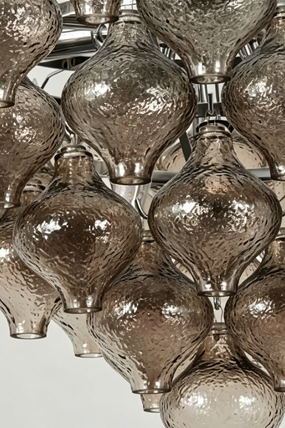 Close-up of the Lucina Tiered Smoked Glass Chandelier showcasing amber-tinted glass bulbs and polished chrome details.