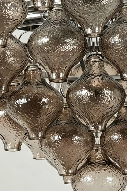 Close-up of the Lucina Tiered Smoked Glass Chandelier showcasing amber-tinted glass bulbs and polished chrome details.