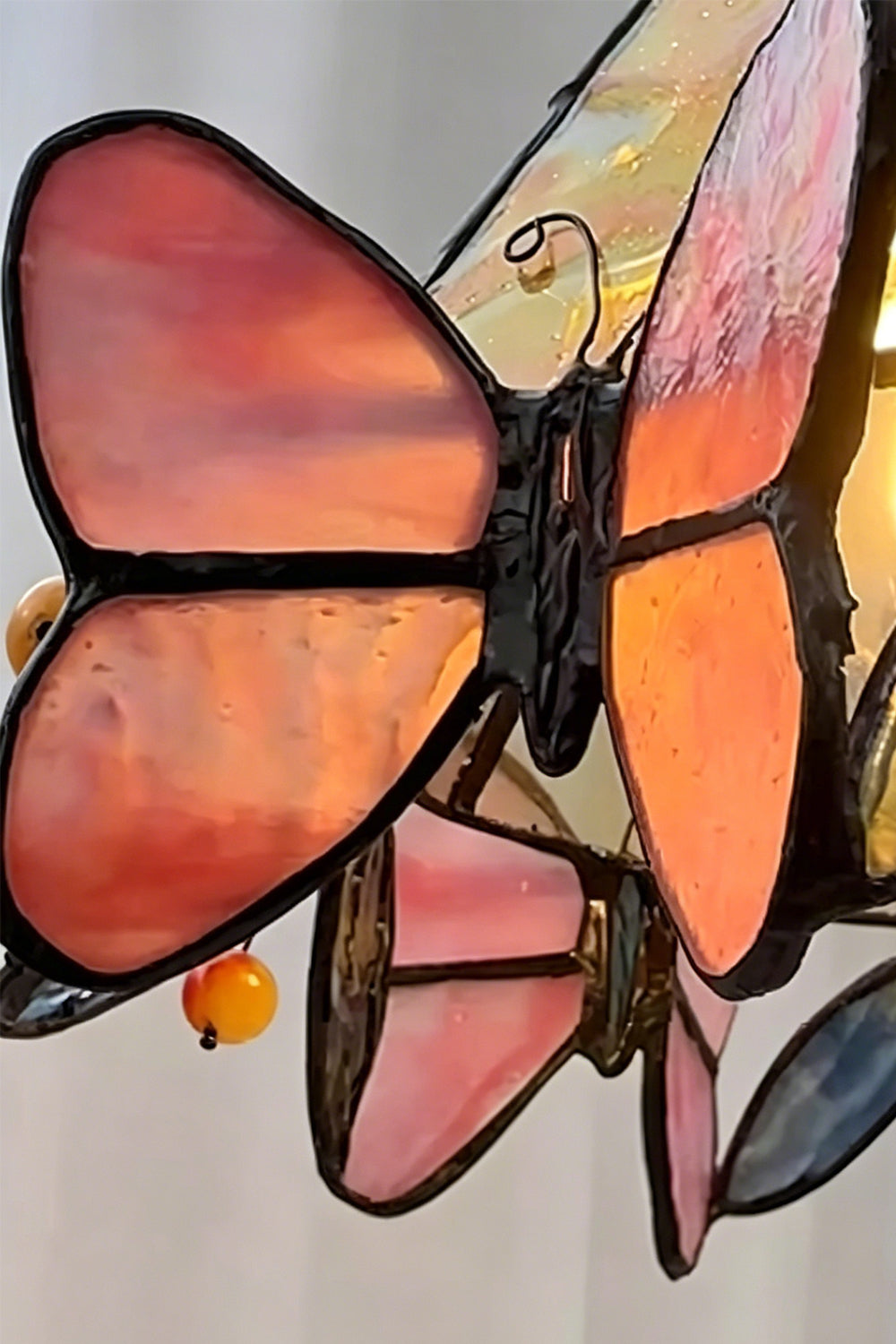 Mariposa Stained Glass Table Lamp | Glass, Metal | Macro focus on a translucent pink and orange stained glass butterfly element along the shade's edge | Detail shot | vexa lamps
