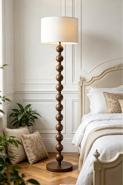 Marlow Stacked Wood Floor Lamp | Wood, Fabric | Illuminating a serene bedroom corner, casting a warm glow next to a white bed and paneled walls with wooden flooring | vexa lamps