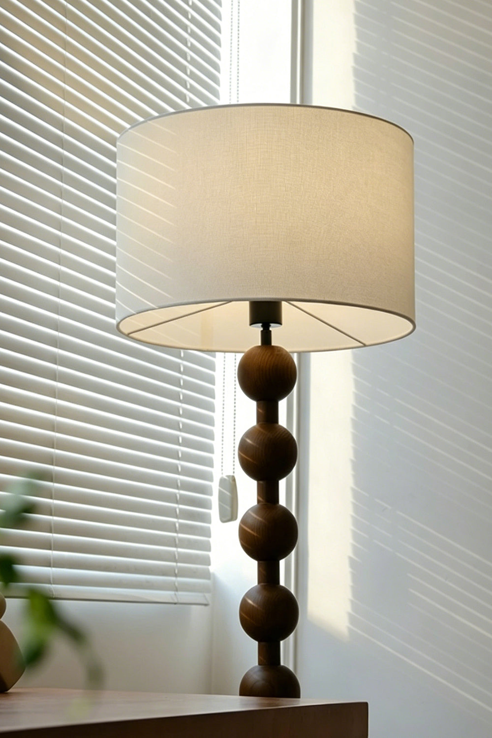 Marlow Stacked Wood Floor Lamp | Wood, Fabric | Upper section of the bobbin floor lamp near a window with slatted blinds, highlighting the interplay of natural light and shadow on the shade | Detail shot | vexa lamps