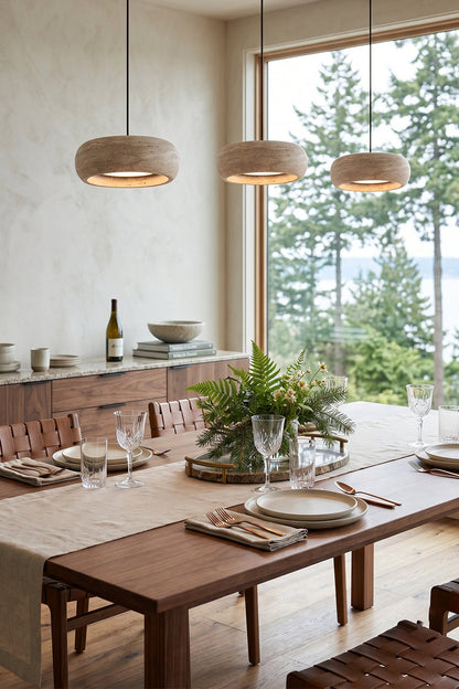 Maro Travertine Donut Pendant Light | Travertine, Metal | Three linear stone pendant fixtures hung above a contemporary wood dining table in a sunlit open-concept home interior | vexa lamps