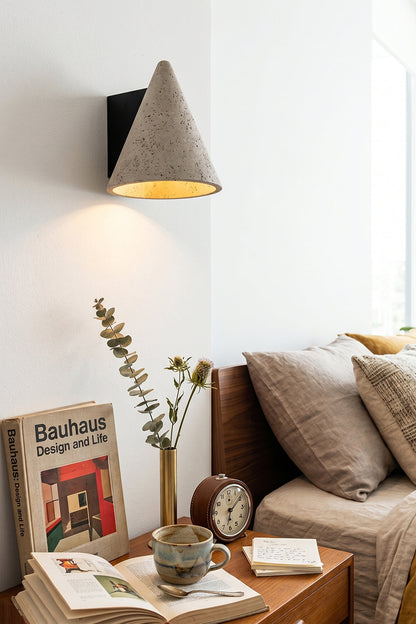 Monolith Cone Travertine Wall Sconce illuminating a cozy bedroom with books and plants.