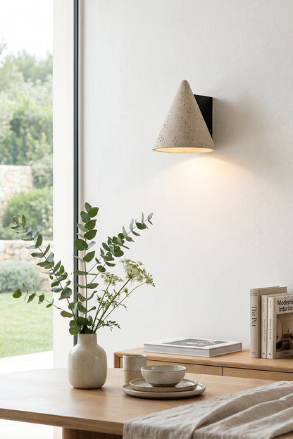 Monolith Cone Travertine Wall Sconce illuminating a modern room with a vase and books on a wooden table.