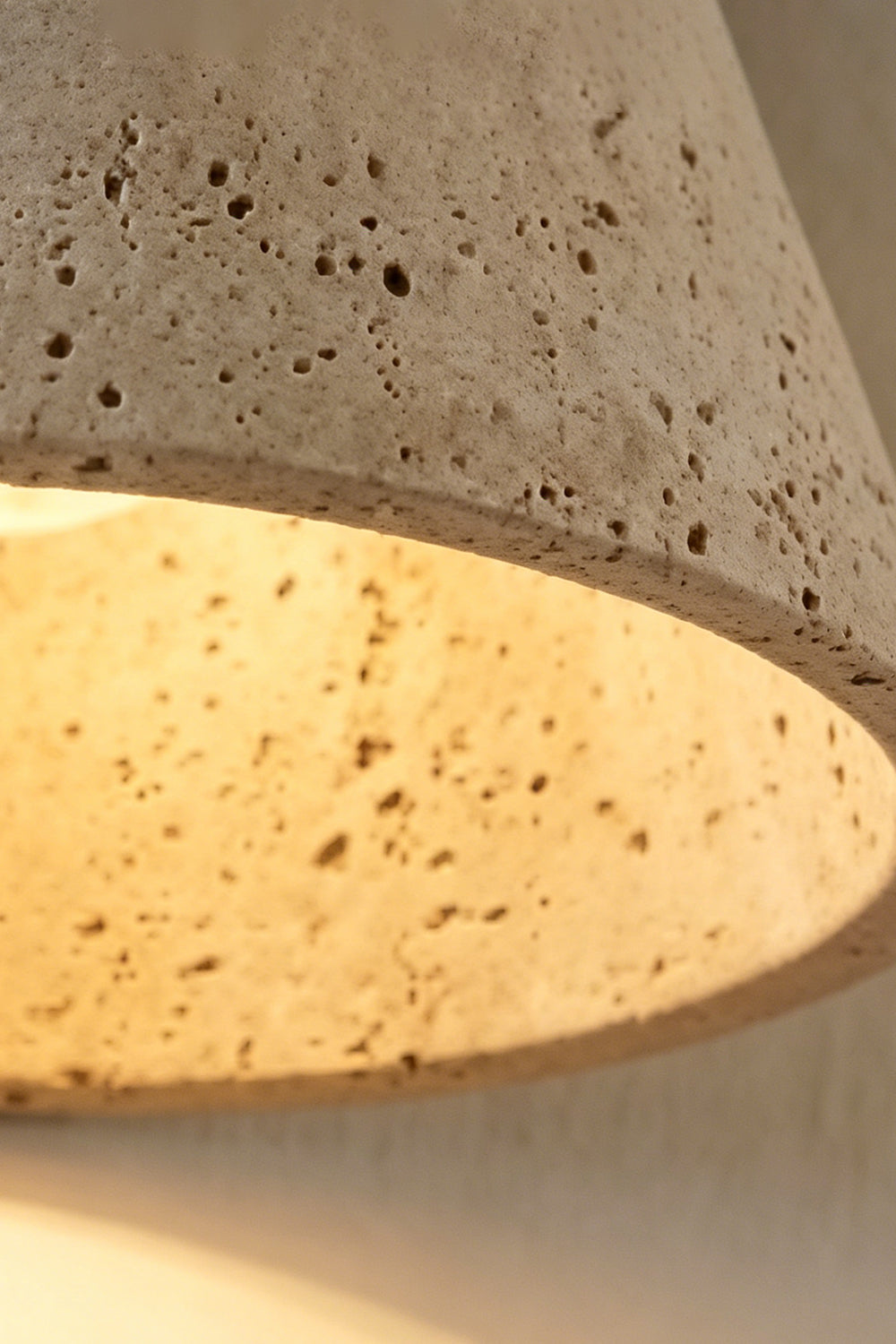 Close-up of the Monolith Cone Travertine Wall Sconce showcasing its textured travertine surface and warm light.