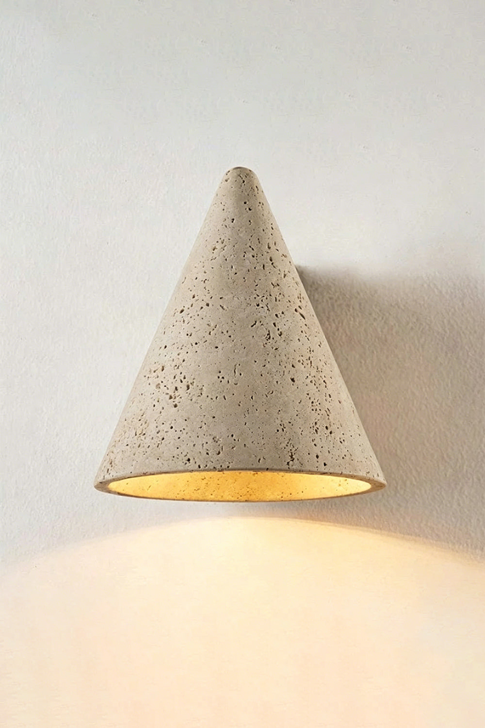 Monolith Cone Travertine Wall Sconce illuminating a wall with its natural yellow travertine texture in a minimalist setting.