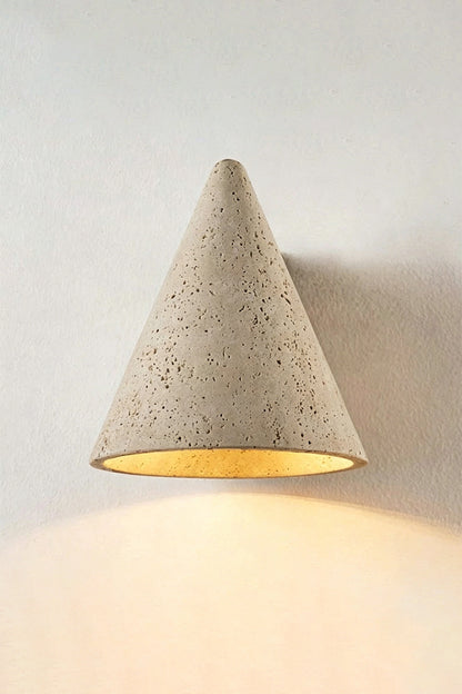 Monolith Cone Travertine Wall Sconce illuminating a wall with its natural yellow travertine texture in a minimalist setting.