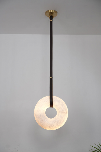 Nerissa Alabaster Ring Leather Pendant Light | Natural Alabaster, Leather and Brass | Single-strap disc variant illuminated softly on a grey wall | vexa lamps