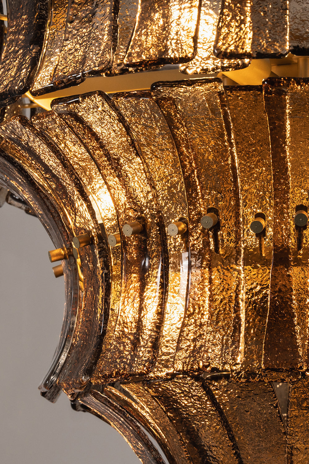 Octavia Sculptural Smoked Glass Chandelier | Illuminated Texture | Macro close-up view of the glowing glass panels highlighting the rich dimpled textures and warm amber gold light refraction | Detail shot | vexa lamps