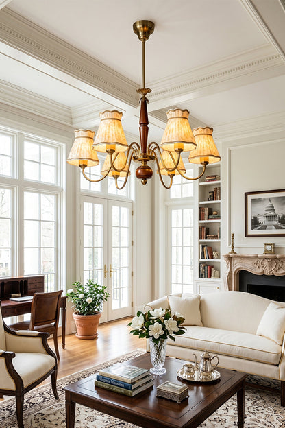 Odette Vintage Pleated Shaded Chandelier | Wood, Brass, Fabric | Hanging as an elegant classical centerpiece in a bright European-style living room featuring white grid windows, a cream sofa, and a fireplace | vexa lamps