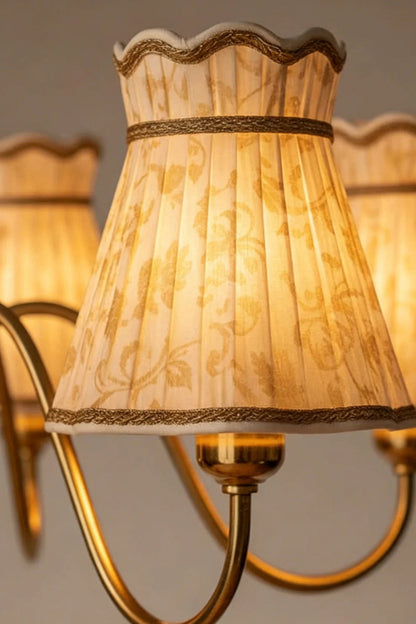 Odette Vintage Pleated Shaded Chandelier | Wood, Brass, Fabric | Macro close-up focus on a single fully illuminated cream fabric pleated shade highlighting its scalloped edge and fine braid trim | Detail shot | vexa lamps