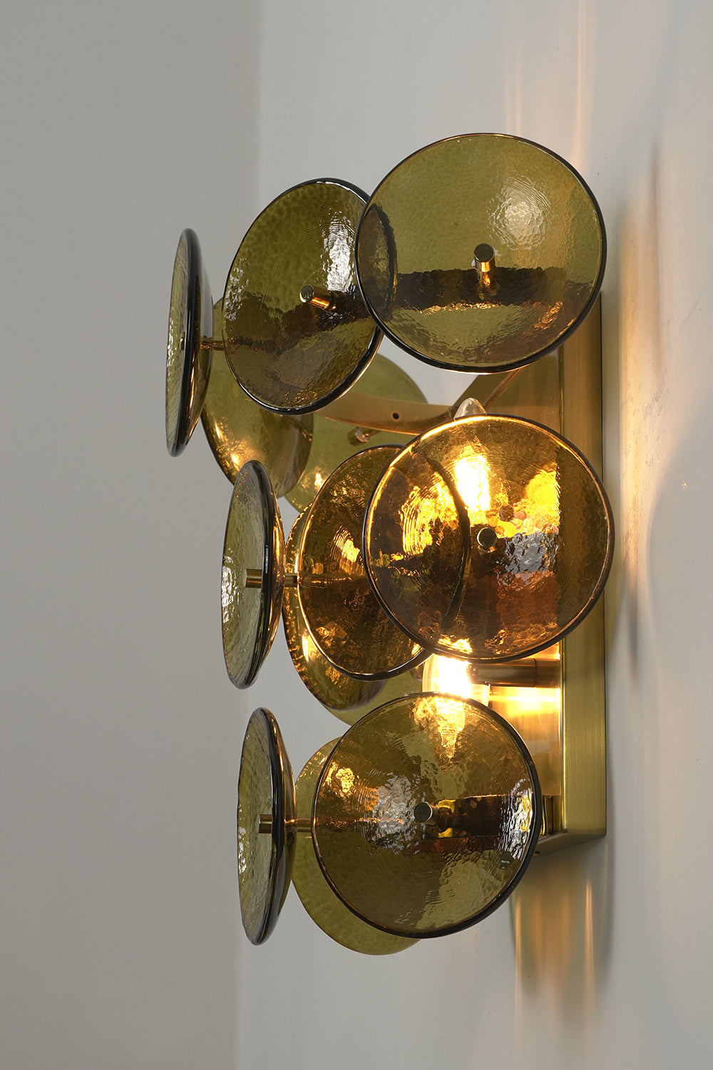 Lit tiered olive green hammered glass wall light | Metal, Glass | Angled lit product view showing tiered layers | vexa lamps