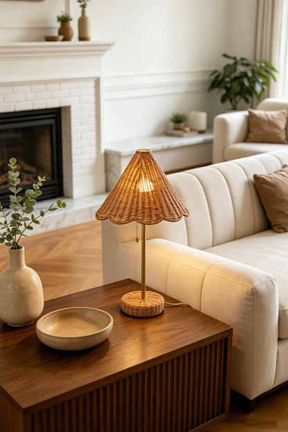 Osrilla Scalloped Rattan Table Lamp | Rattan, Brass | Fully illuminated bohemian rattan table lamp providing warm ambient light on a wooden end table next to a cream sectional sofa near a fireplace | vexa lamps