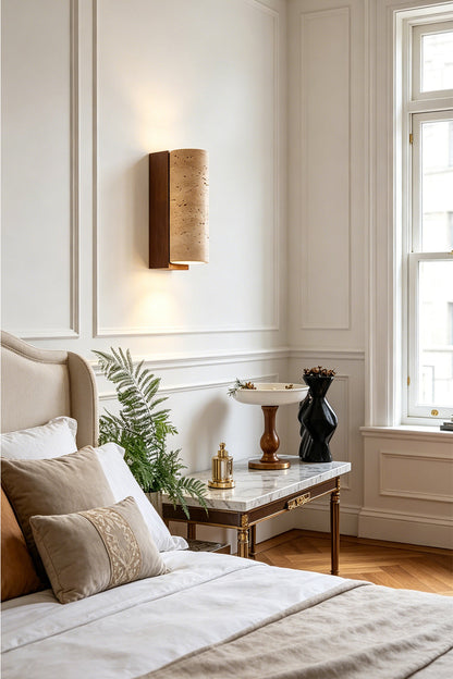 Outcrop Beige Travertine Wall Sconce | Travertine, Metal | Mounted as an elegant bedside accent light casting a warm upward and downward glow on a white wall next to a bed with a cream headboard | vexa lamps