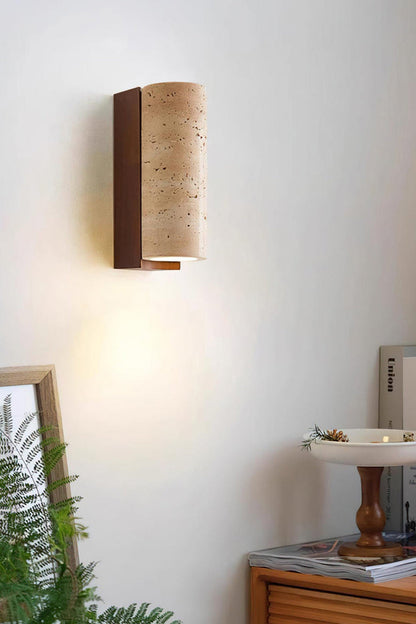 Outcrop Beige Travertine Wall Sconce | Travertine, Metal | Cozy indoor scene of the lit architectural stone sconce casting an organic glow near green house plants and a wooden shelf | vexa lamps