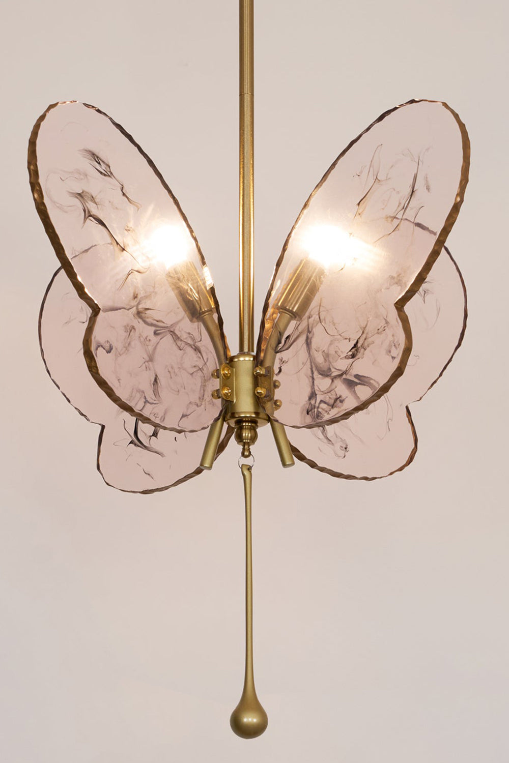 Papillon Glass Butterfly Pendant Lamp | Glass, Metal | Frontal straight-on view of the illuminated pink glass butterfly fixture throwing a warm backlight halo on a neutral wall | vexa lamps