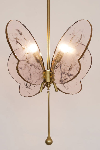 Papillon Glass Butterfly Pendant Lamp | Glass, Metal | Frontal straight-on view of the illuminated pink glass butterfly fixture throwing a warm backlight halo on a neutral wall | vexa lamps