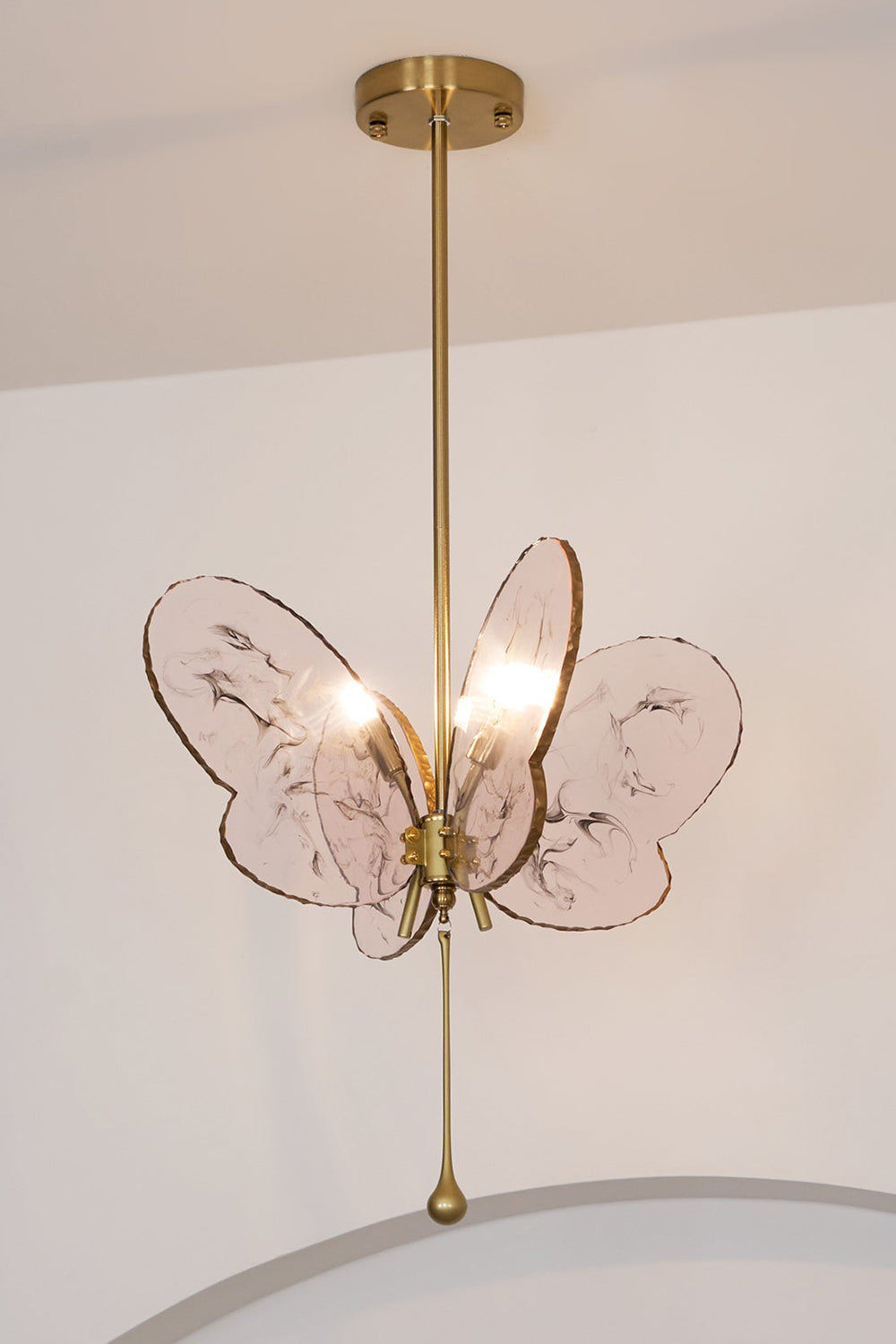Papillon Glass Butterfly Pendant Lamp | Glass, Metal | Low-angle view looking up at the fully lit pink butterfly hanging light against a plain white wall | vexa lamps
