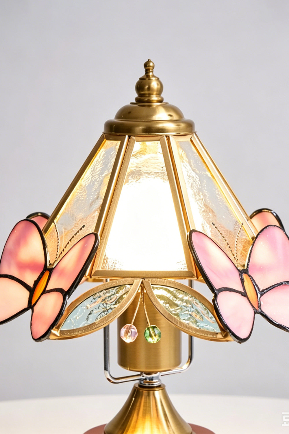 Papillon Heirloom Stained Table Lamp | Wood, Glass, Metal | Close-up frontal view of the lit stained glass shade highlighting the pink butterfly wings and brass frame | Detail shot | vexa lamps