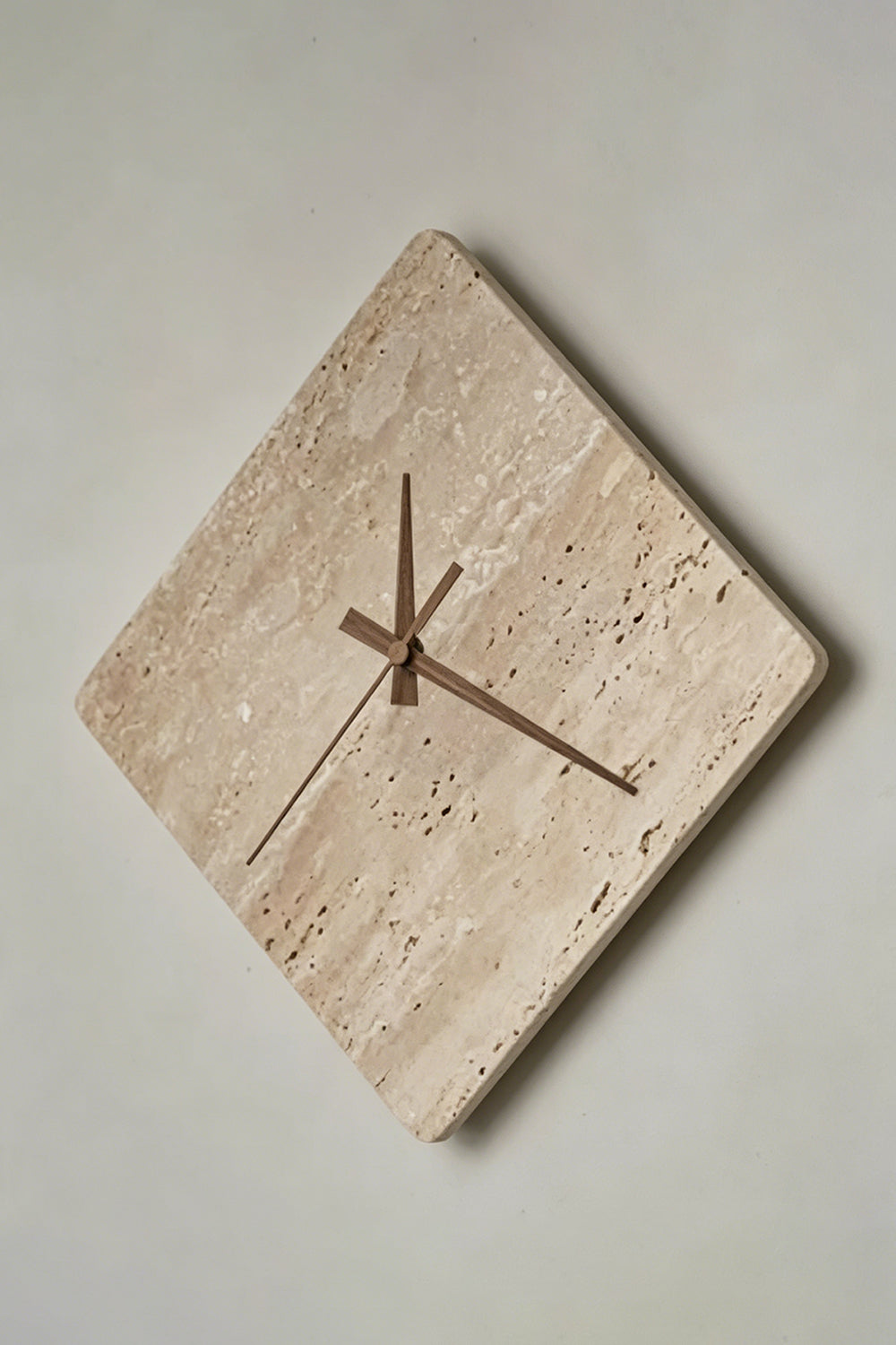 Petra Compass Travertine Backlit Wall Lamp | Travertine, Iron | Angled frontal view of the unlit travertine clock-lamp displaying its natural porous stone surface against a grey wall | Detail shot | vexa lamps