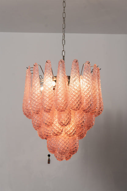 Amara Blush Cascading Glass Chandelier | Glass, Metal | Medium shot of the lit tiered chandelier radiating a soft rose glow against a light grey background | vexa lamps